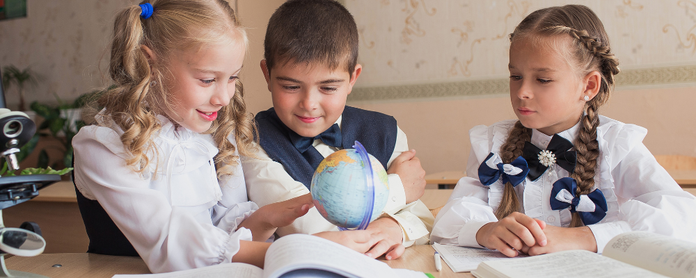 Schulkinder an einem Schultisch, die auf einen Globus schauen