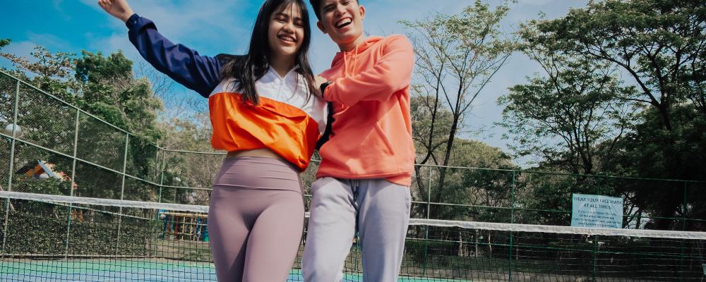 Zwei junge Menschen in sportlich-lässigem Outfit auf einem Tennisplatz
