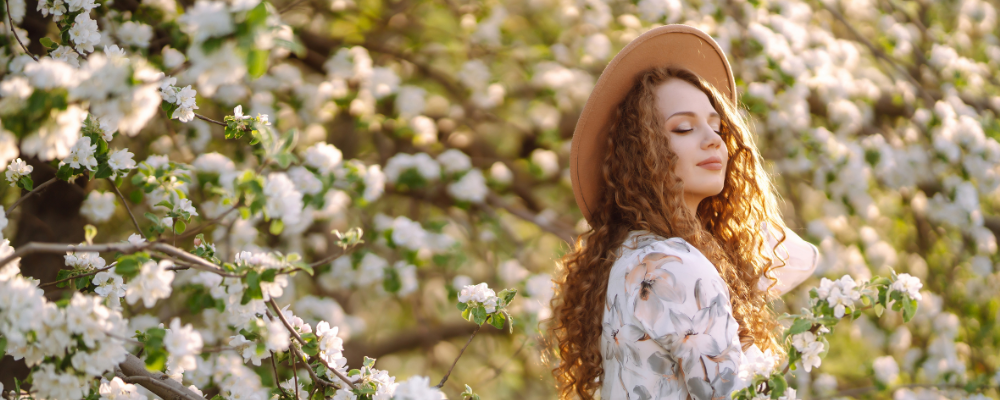 Frau in Frühlingskleidung mit Hut steht zwischen blühenden Baumästen