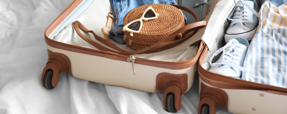 Beigefarbener Koffer mit Hemd, Jeans, Tasche und Sonnenbrille.