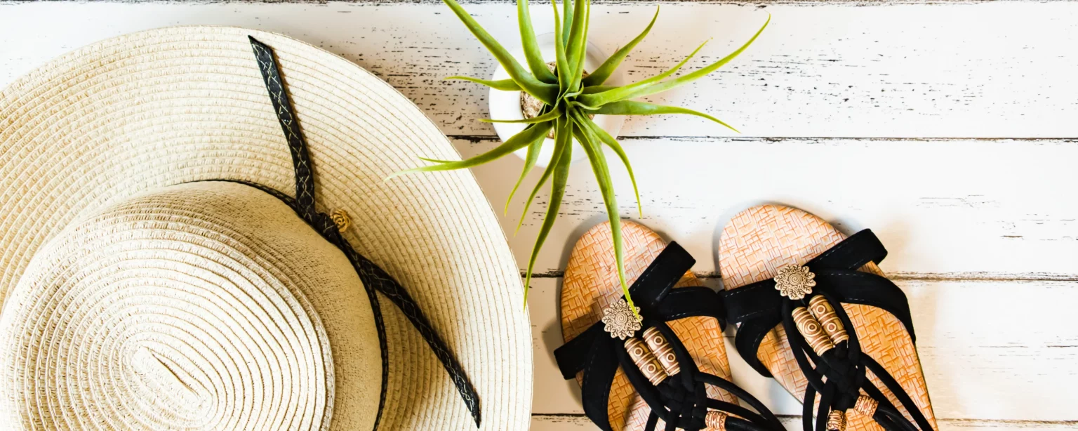 Strohhut und Sandalen als Sommer-Accessoires auf hellem Holzboden
