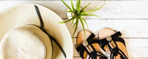Strohhut und Sandalen als Sommer-Accessoires auf hellem Holzboden