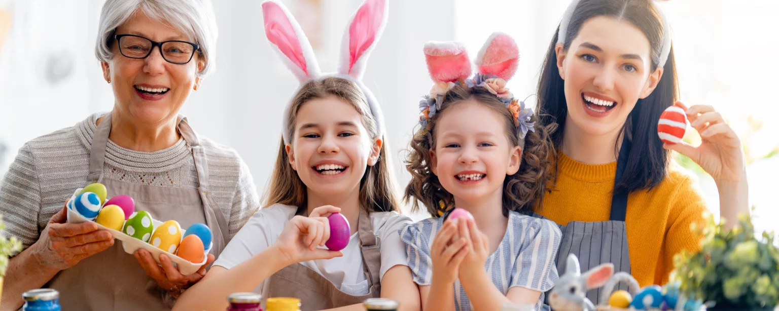 Großmutter, Mutter und zwei Kinder bemalen gemeinsam bunte Ostereier zu Ostern